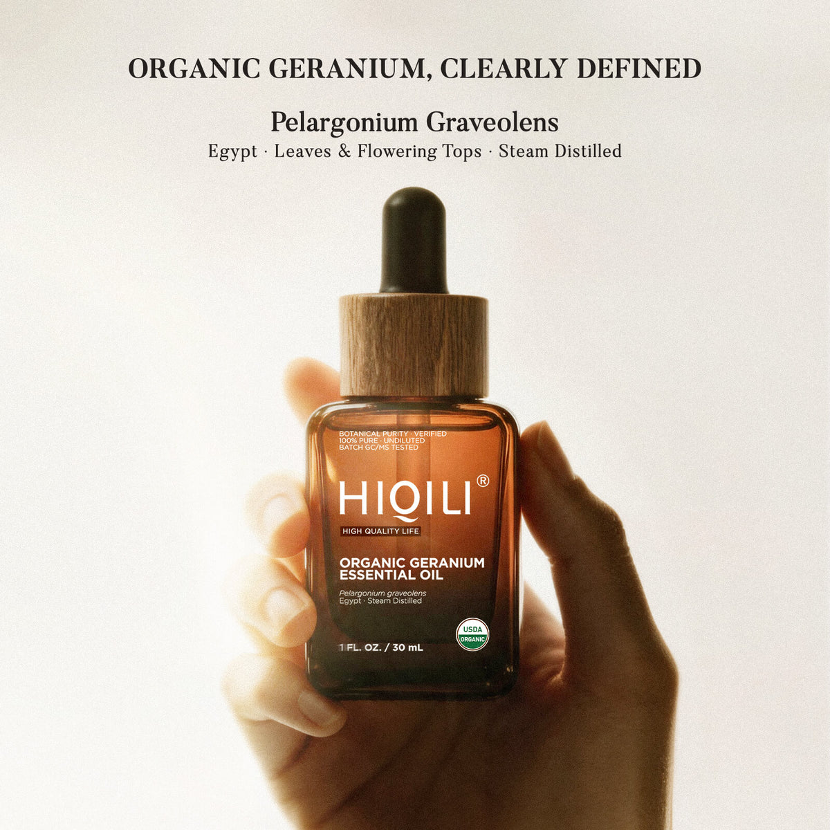 Hand holding a HIQILI organic geranium essential oil bottle labelled Pelargonium graveolens from Egypt