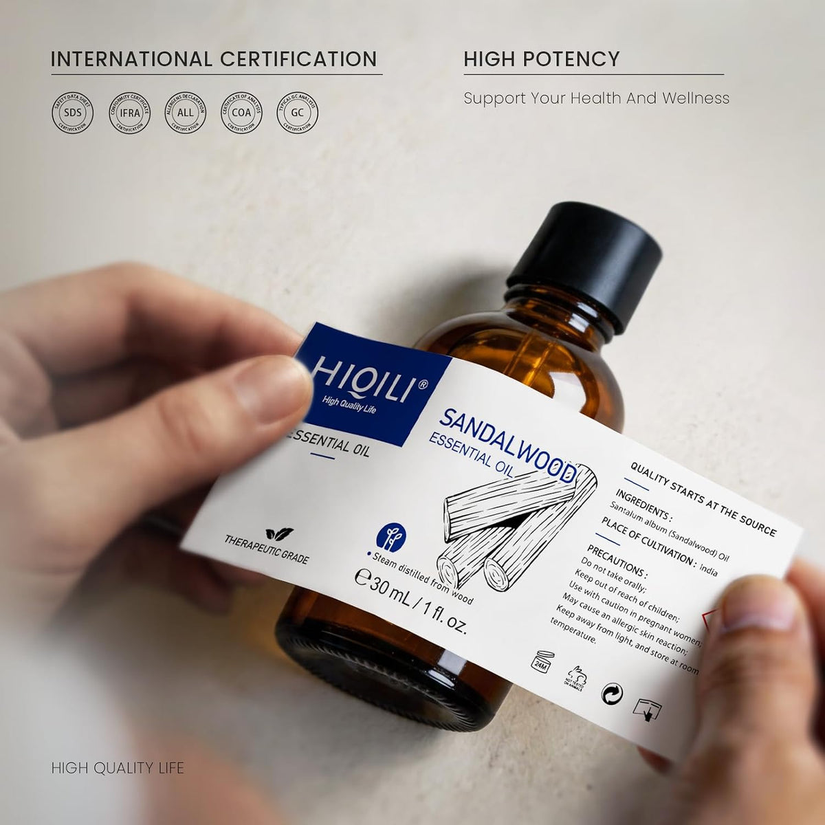 Hand holding a HIQILI Sandalwood Essential Oil bottle with an international certification badge
