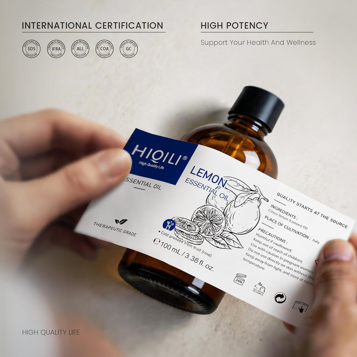 Hand holding a HIQILI Lemon Essential Oil bottle with an international certification badge