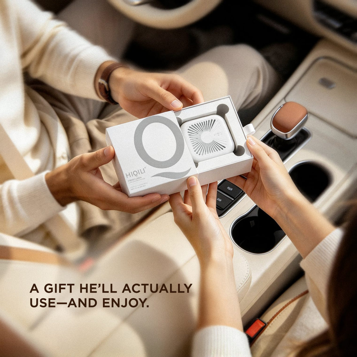 Open HIQILI gift box holding the ivory white air freshener, passed between two hands inside a car