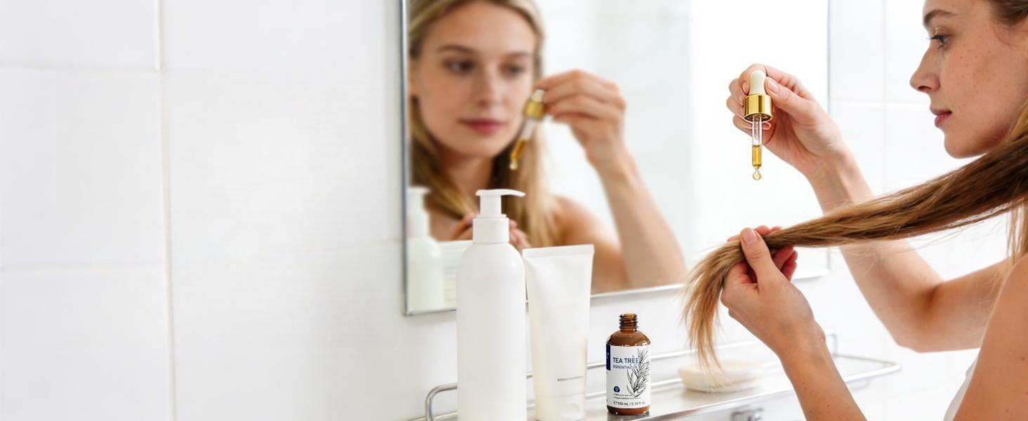 Woman looking in the mirror, applying a nourishing blend of pure tea tree essential oil and carrier oil to her hair ends for natural shine and split-end repair.