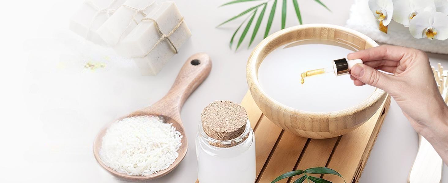 Woman making DIY handmade soap by adding pure vanilla essential oil into a wooden bowl of melted soap base, surrounded by white orchids and natural ingredients.