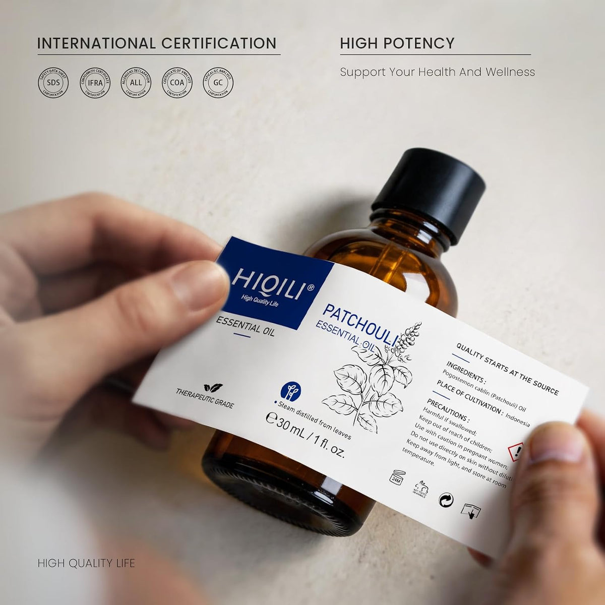 Hand holding a HIQILI Patchouli Essential Oil bottle with an international certification badge