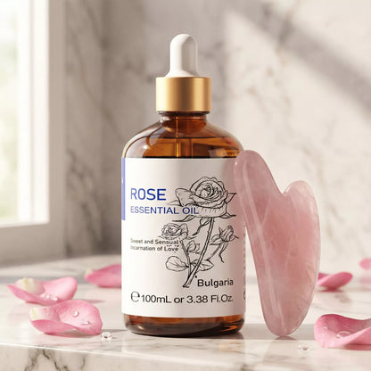 A bottle of Rose Essential Oil next to a pink quartz gua sha tool and fresh rose petals on a marble vanity, representing a luxury anti-aging skincare routine.